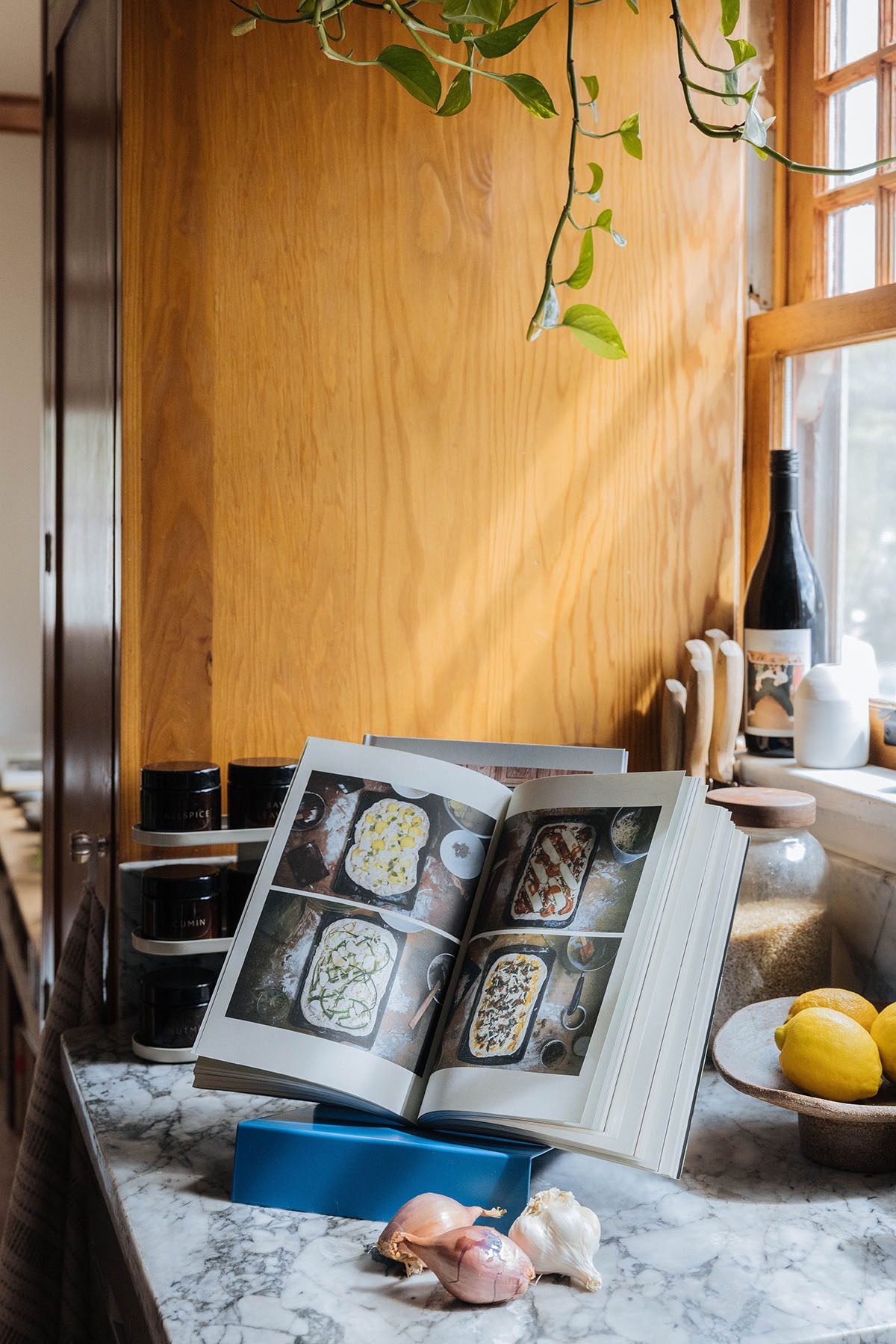 Upton LP Stand in blue. Modern and minimalist tabletop steel vinyl record holder made for the storage, organization, and display 50 albums. Shown being used as a cookbook holder in a modern sunny kitchen with wine and garlic and lemons.