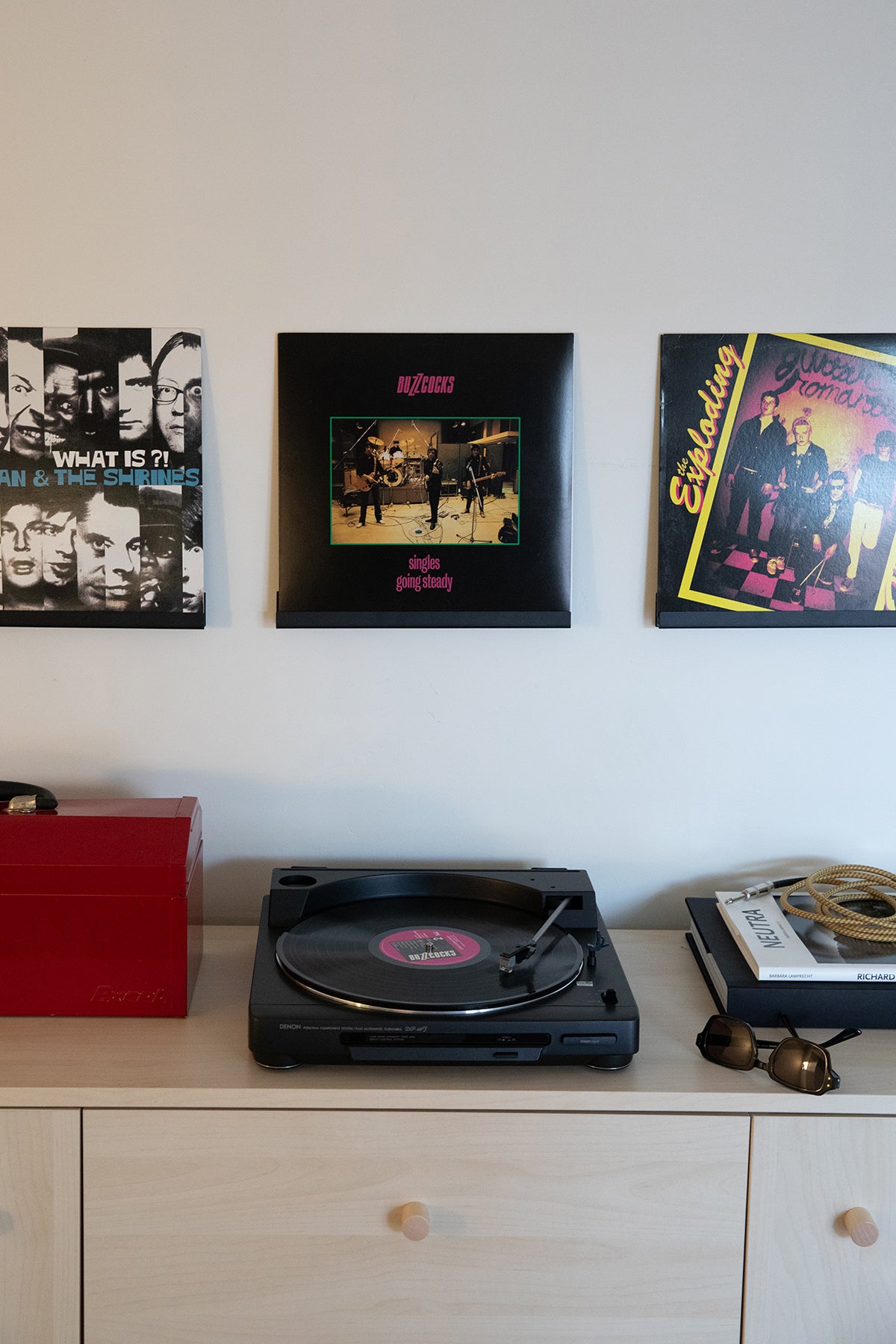Upton LP Wall Display in black. Modern and minimalist steel wall shelf made to hang vinyl record sleeves on a wall. Shown holding three records on a white wall over a tabletop record player.