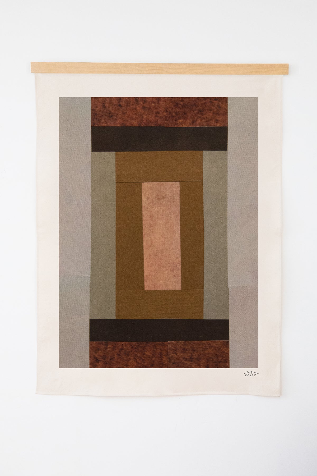 The Rouen is an original art print on 100% cotton canvas from Michael Upton. Featuring an abstract quilt-like collage design in muted earth tones, the Rouen is a large format modern wall hanging. Shown here with a wooden hanging bar on a white background.