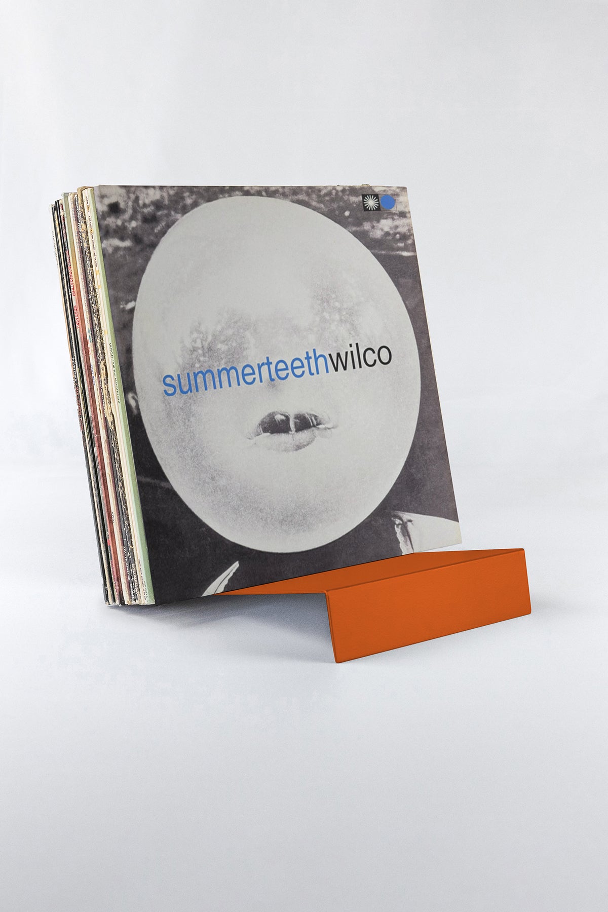 Upton LP Stand in burnt orange. Modern and minimalist tabletop steel vinyl record holder made for storage, organization, and display of 50 albums on a white background. Holding a stack of records with a Wilco album in front.