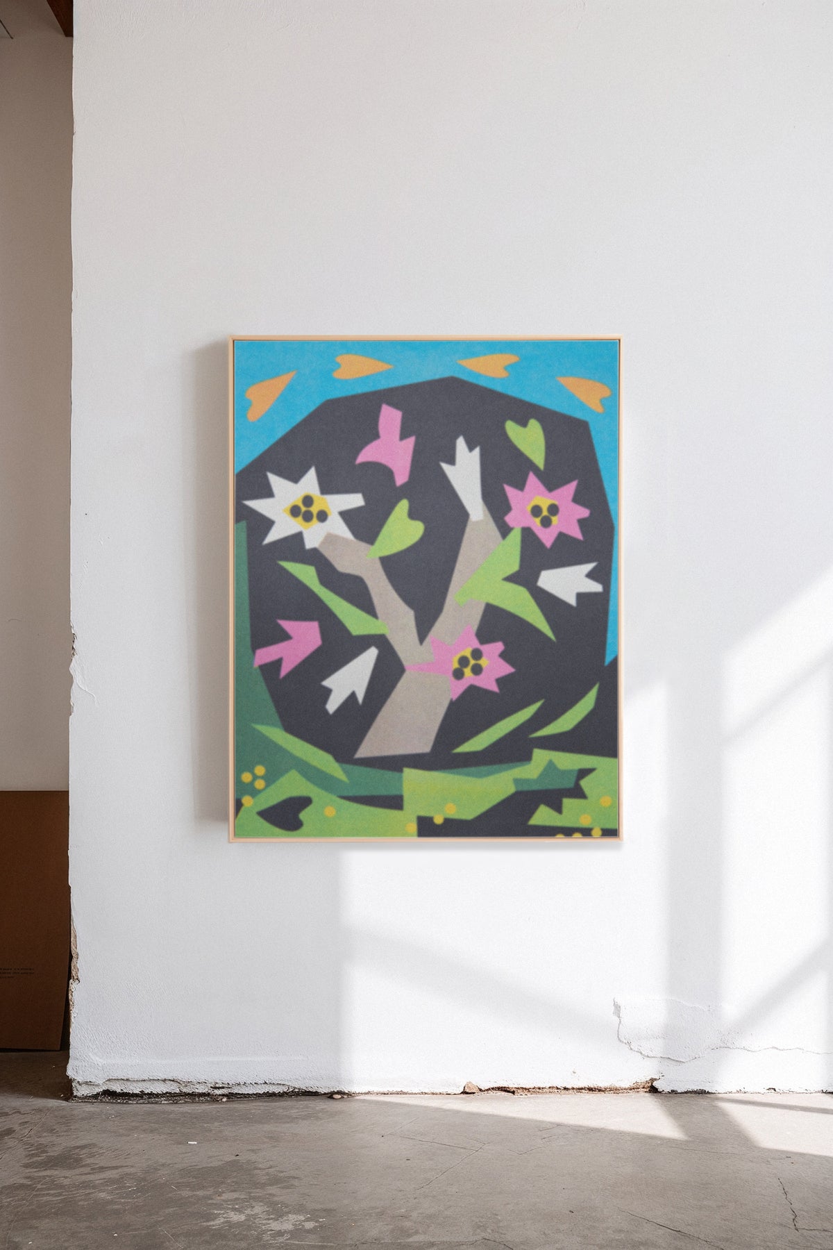 Magnolia in Bloom by Sunroom Studios x Upton, a custom framed art print on 100% cotton canvas. Large cut paper collage featuring a flowering magnolia tree in bold geometric shapes and bright colors. Originally created as a risograph print. Shown in a gallery setting with concrete floors and natural light.