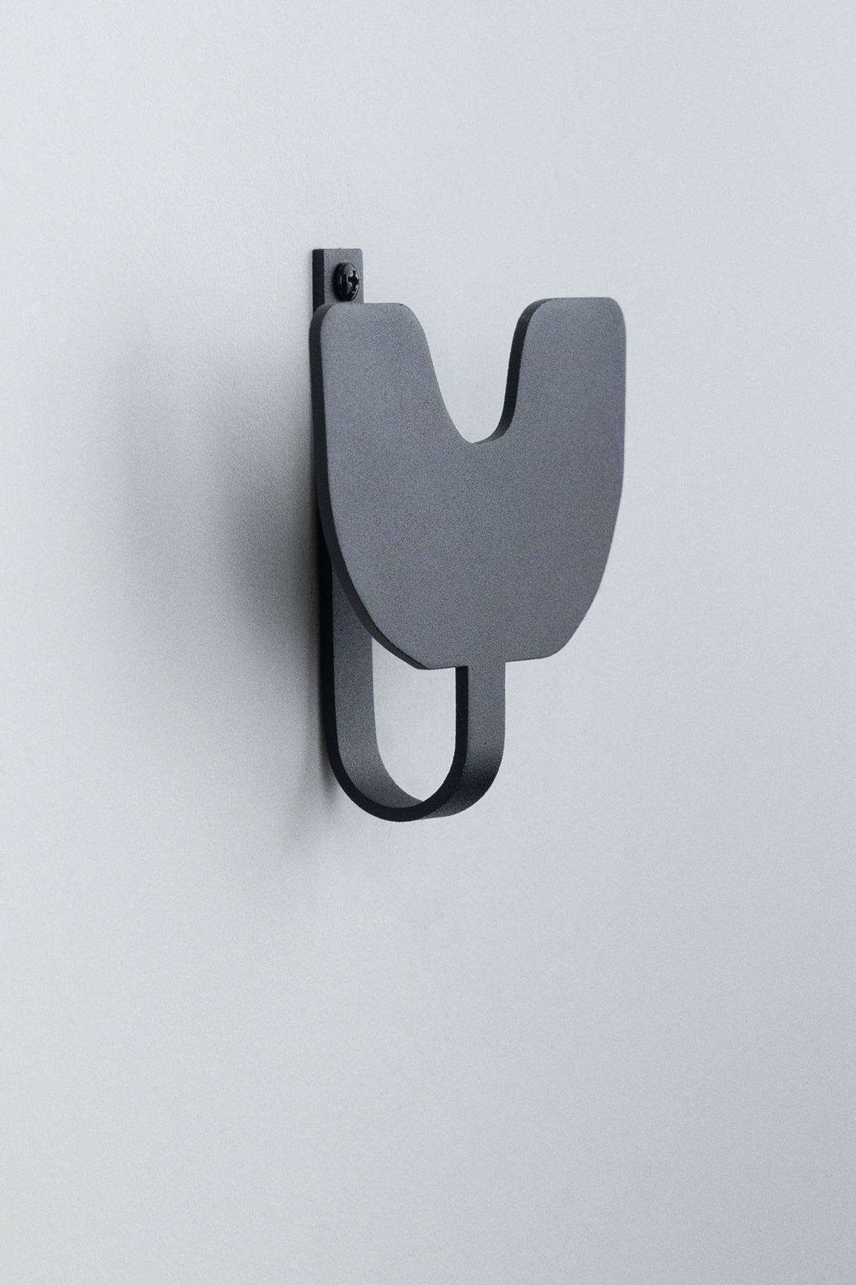 Upton Abra Wall Hook in black. A sculptural decorative steel wall hook with a black color scheme with a unique abstract shape, designed to hang bags, coats, towels, hats, and more. Shown here on a white background.