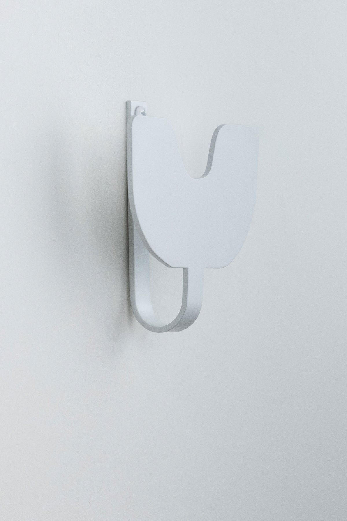 Upton Abra Wall Hook in white. A sculptural decorative steel wall hook with a white color scheme with a unique abstract shape, designed to hang bags, coats, towels, hats, and more. Shown here on a white background.