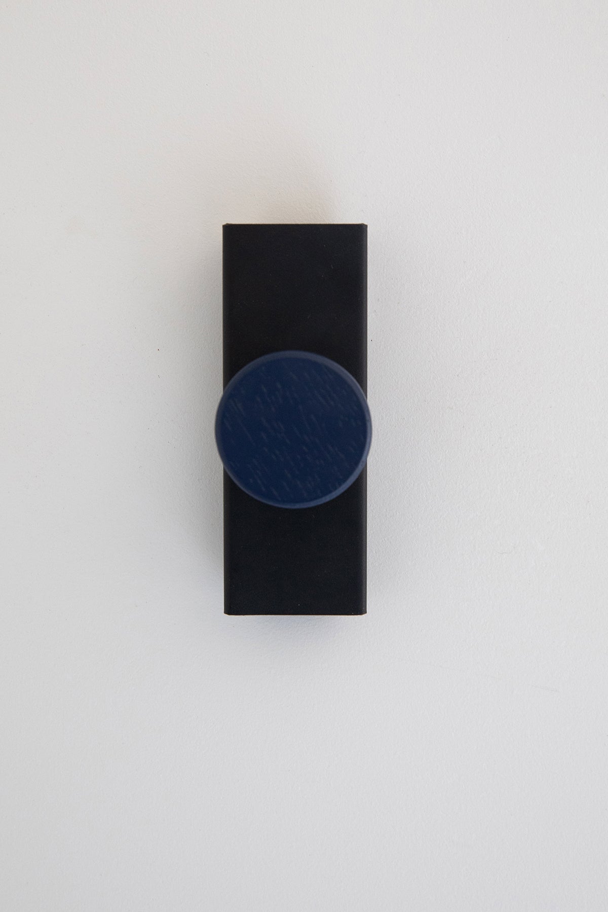 Upton Canal Wall Hook in black/navy. A sculptural decorative steel and wood wall hook with a black and navy blue color scheme with a unique shape, designed to hang bags, coats, towels, hats, and more. Shown here on a white background.