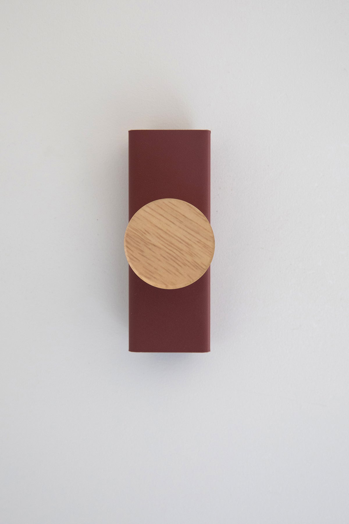 Upton Canal Wall Hook in rose. A sculptural decorative steel and wood wall hook with a rose (red/pink) color scheme with a unique shape, designed to hang bags, coats, towels, hats, and more. Shown here on a white background.