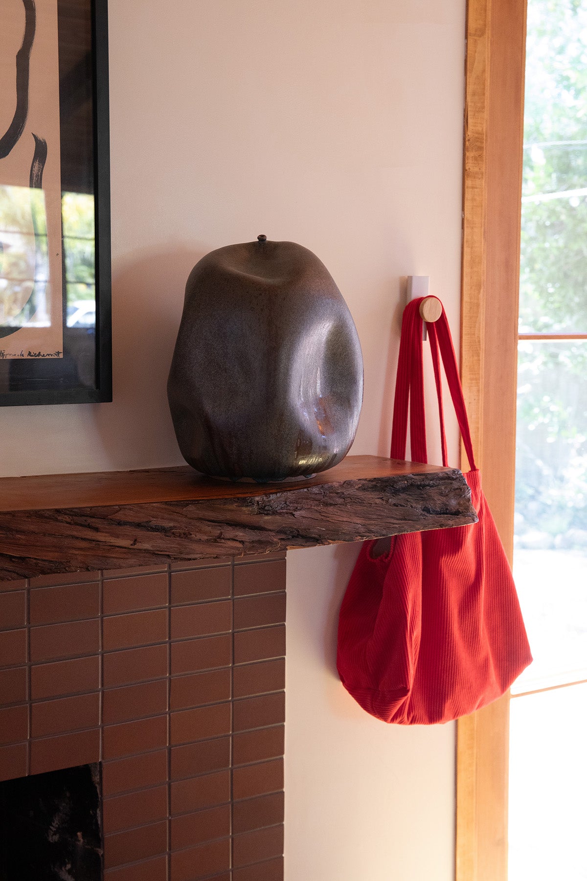 Upton Canal Wall Hook in white. A sculptural decorative steel and wood wall hook with a white color scheme with a unique shape, designed to hang bags, coats, towels, hats, and more. Shown here in an elevated interior holding a red tote bag with handmade ceramic vase.