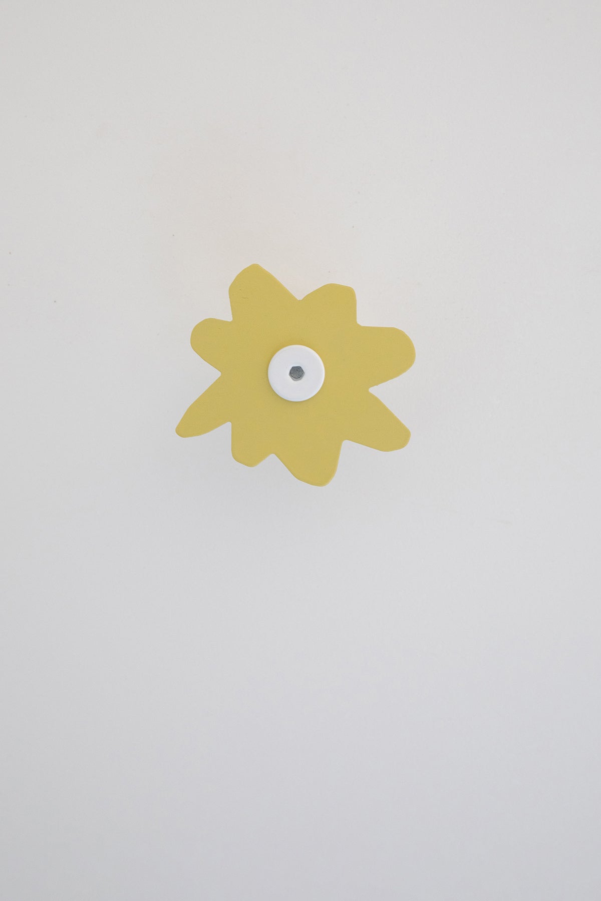 Upton Fleur Wall Hook in pale yellow. A sculptural decorative steel wall hook with a pale yellow color scheme with a unique abstract flower shape, designed to hang bags, coats, towels, hats, and more. Shown here on a white background.