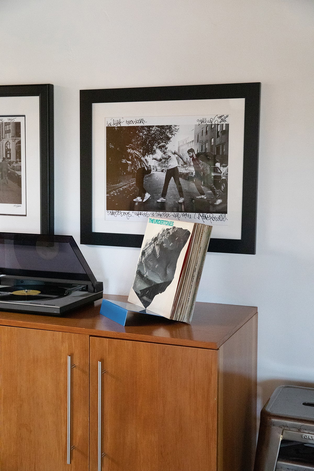 Upton LP Stand in blue. Modern and minimalist tabletop steel vinyl record holder made for the storage, organization, and display 50 albums. Shown holding a stack of records on a wooden media cabinet with a record player in a modern interior.