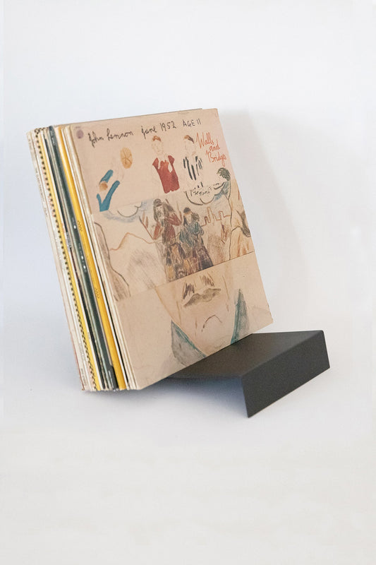 Upton LP Stand in black. Modern and minimalist tabletop steel vinyl record holder made for the storage, organization, and display 50 albums. Shown holding a stack of records with a John Lennon album on a white background.