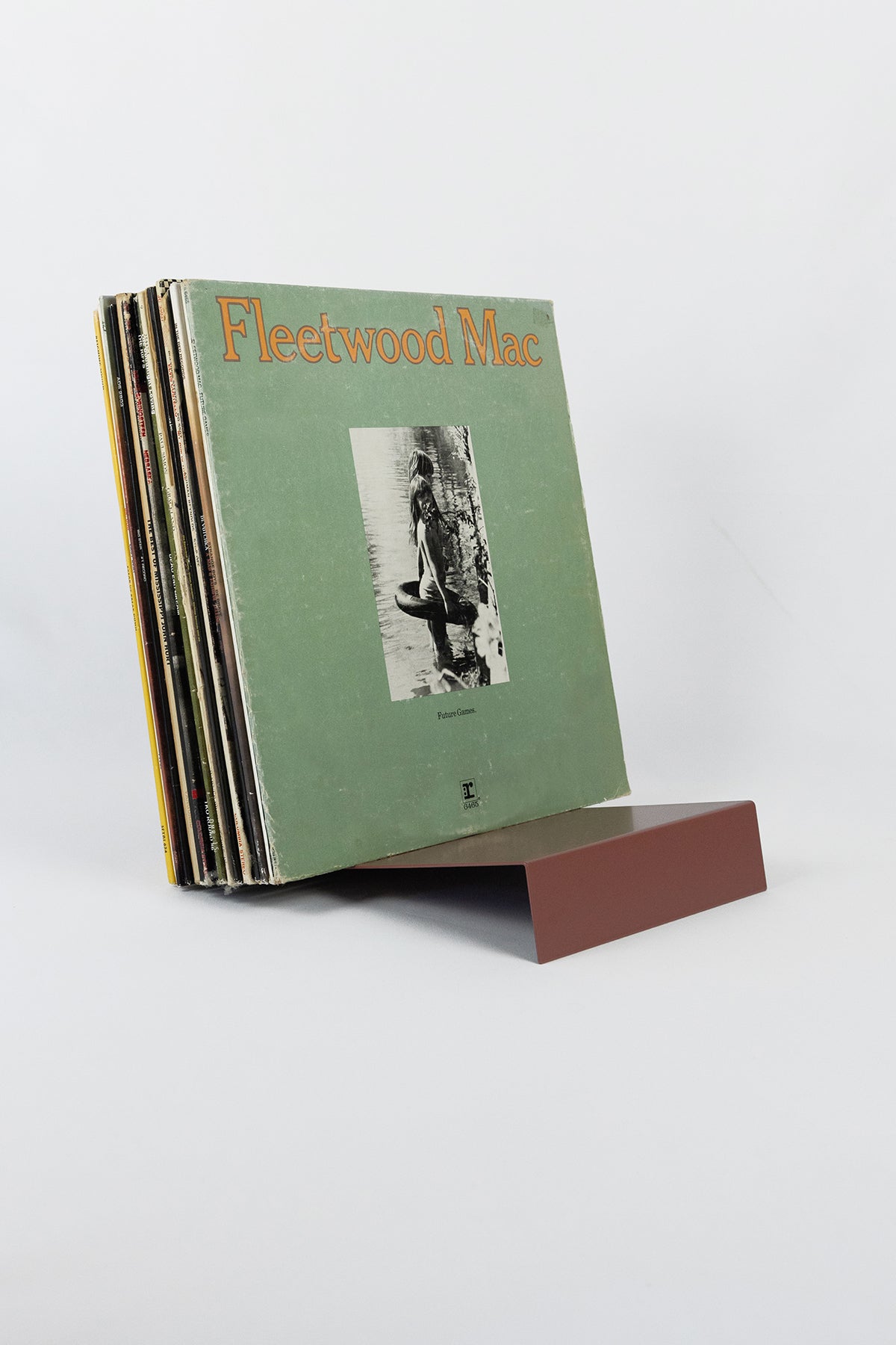 Upton LP Stand in rose (pink/red). Modern and minimalist tabletop steel vinyl record holder made for storage, organization, and display of 50 albums. Shown holding a Fleetwood Mac album on a white background.