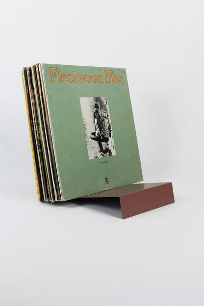 Upton LP Stand in rose (pink/red). Modern and minimalist tabletop steel vinyl record holder made for storage, organization, and display of 50 albums. Shown holding a Fleetwood Mac album on a white background.