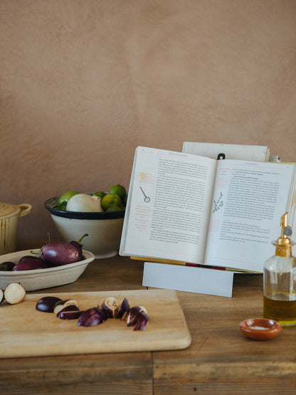 Upton LP Stand in white. Modern and minimalist tabletop steel vinyl record holder made for the storage, organization, and display 50 albums. Shown being used as a cookbook stand with ingredients on a wooden table in a rustic kitchen.