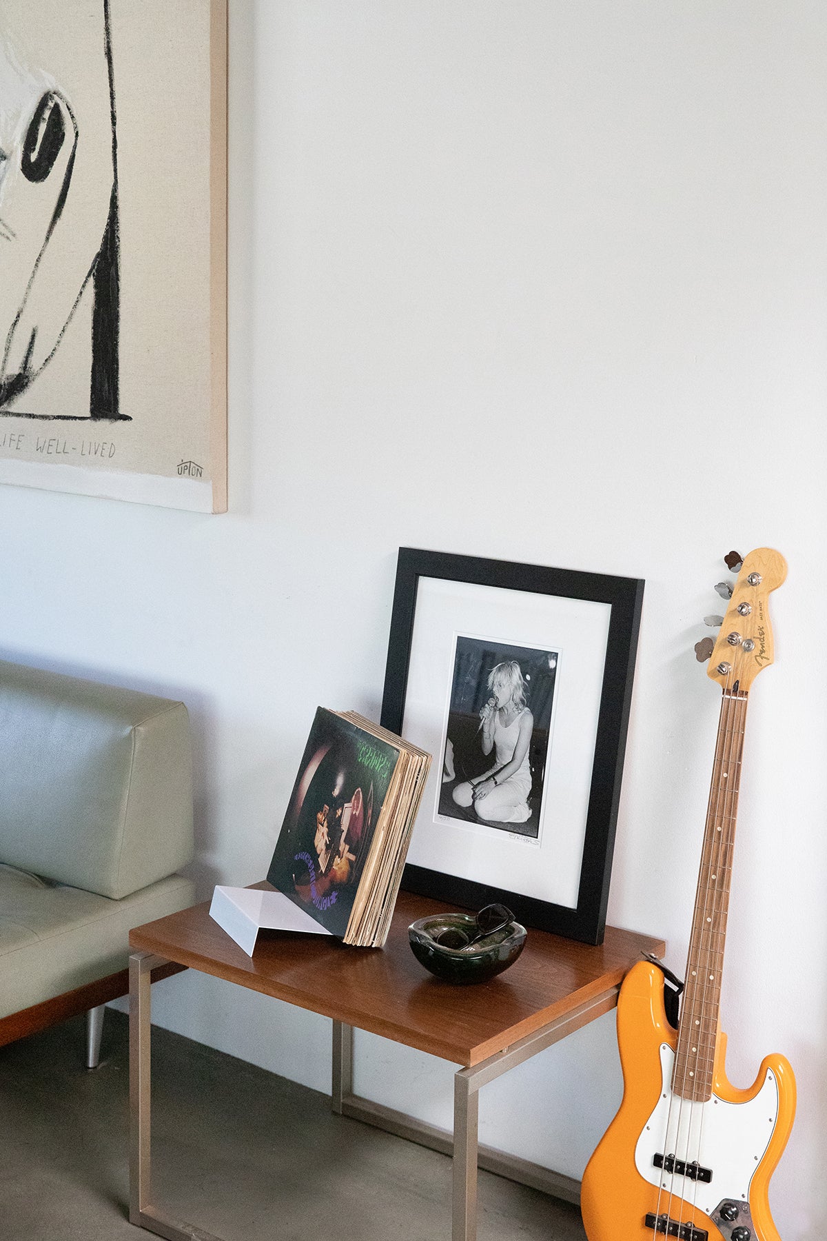 Upton LP Stand in white. Modern and minimalist tabletop steel vinyl record holder made for the storage, organization, and display 50 albums. Shown holding a stack of albums with an orange bass guitar leaning against a wall with framed pictures and a table in a modern interior.