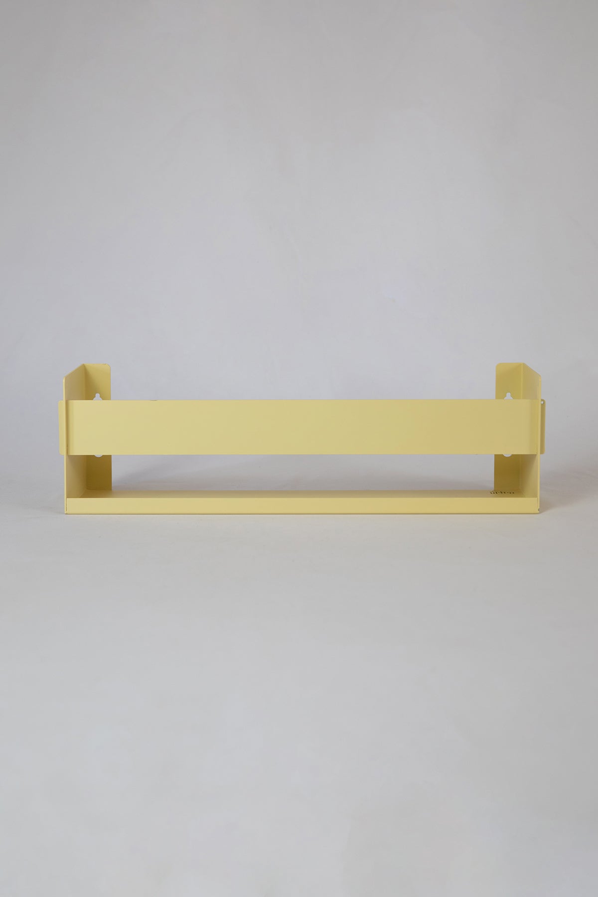 Upton Wall-Mounted Metal Shelf in butter yellow. With a bright, modern design and made from powder coated steel, this minimalist floating wall shelf is designed to be used as a bookshelf, magazine rack, cookbook holder, spice rack, knick knack shelf, or anything else you can think up. Shown on a white background.