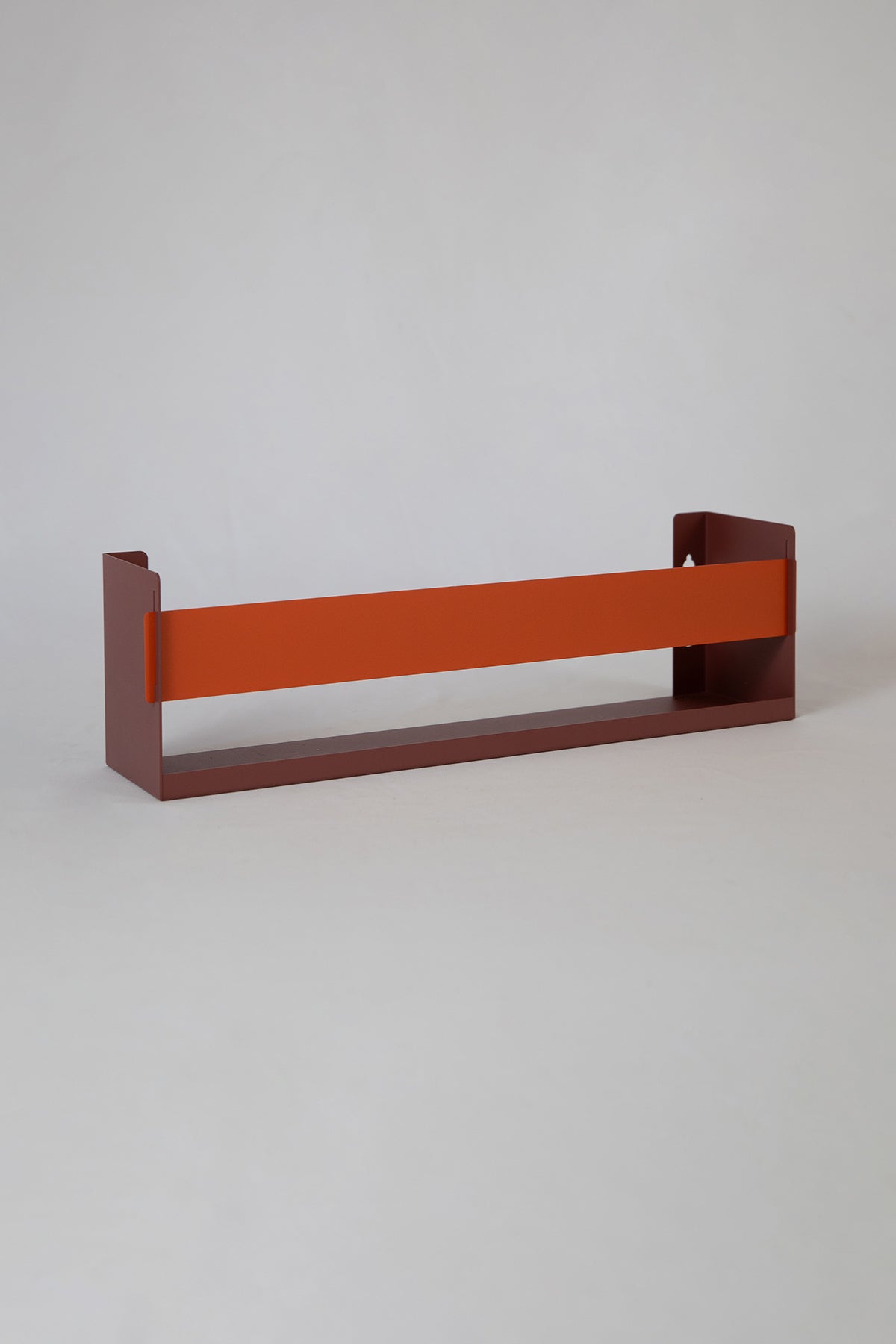 Upton Wall-Mounted Metal Shelf in rose (red/pink) and burnt orange. With a bright, modern design and made from powder coated steel, this minimalist floating wall shelf is designed to be used as a bookshelf, magazine rack, cookbook holder, spice rack, knick knack shelf, or anything else you can think up. Shown on a white background.