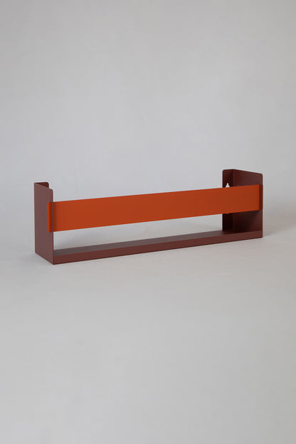 Upton Wall-Mounted Metal Shelf in rose (red/pink) and burnt orange. With a bright, modern design and made from powder coated steel, this minimalist floating wall shelf is designed to be used as a bookshelf, magazine rack, cookbook holder, spice rack, knick knack shelf, or anything else you can think up. Shown on a white background.