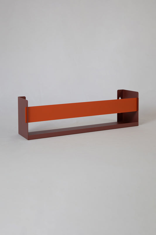 Upton Wall-Mounted Metal Shelf in rose (red/pink) and burnt orange. With a bright, modern design and made from powder coated steel, this minimalist floating wall shelf is designed to be used as a bookshelf, magazine rack, cookbook holder, spice rack, knick knack shelf, or anything else you can think up. Shown on a white background.