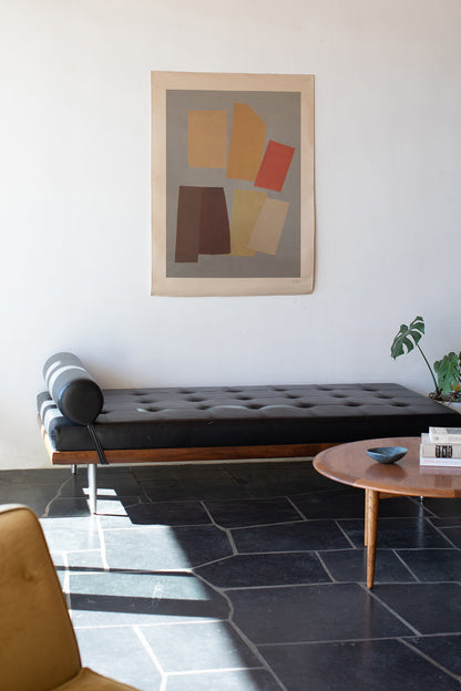 The Aluette is an original art print on 100% cotton canvas from Michael Upton. Featuring an abstract collage of overlapping geometric shapes in rich jewel tones, the Aluette is a large format modern wall hanging. Shown here in a modern living room with black sofa and wooden table.