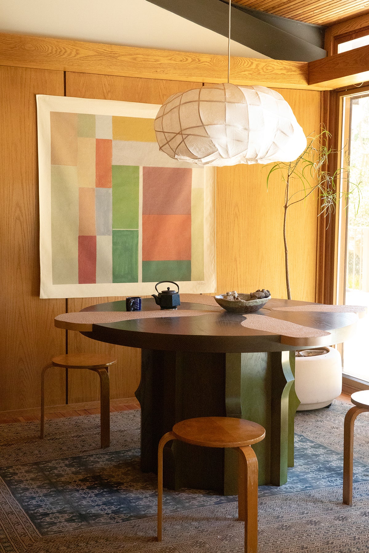 The Mata is an original art print on 100% cotton canvas from Michael Upton. Featuring an architectural abstract design in earth tones, the Mata is a large format modern wall hanging. Shown here in a modern dining room with handmade wooden table and pendant light.