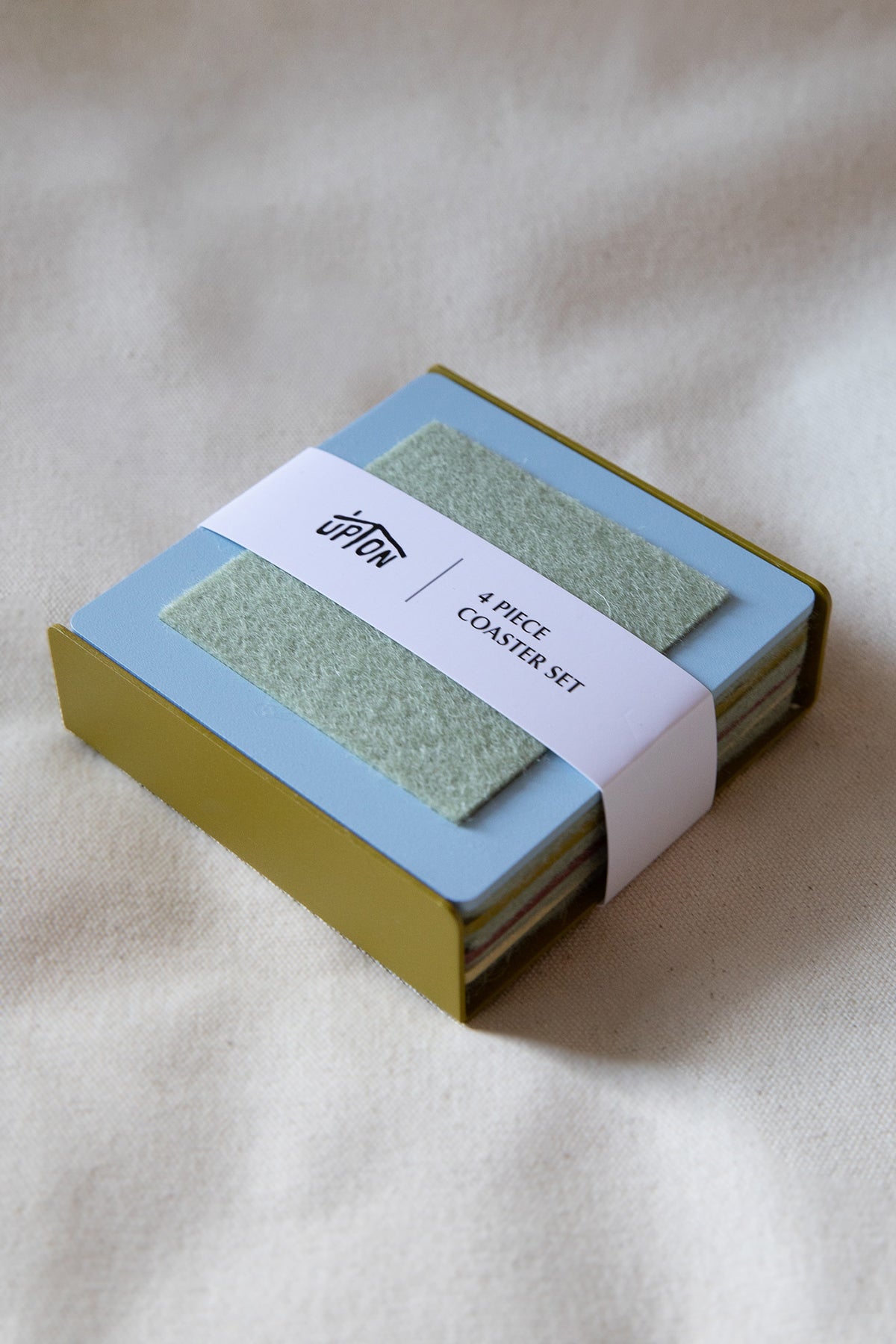 Upton Coaster Set. A bright, colorful 4-piece Coaster Set designed to protect your surfaces from water marks and spills. Crafted from powder coated steel and felt made from 100% New Zealand wool. Shown here on a white background.
