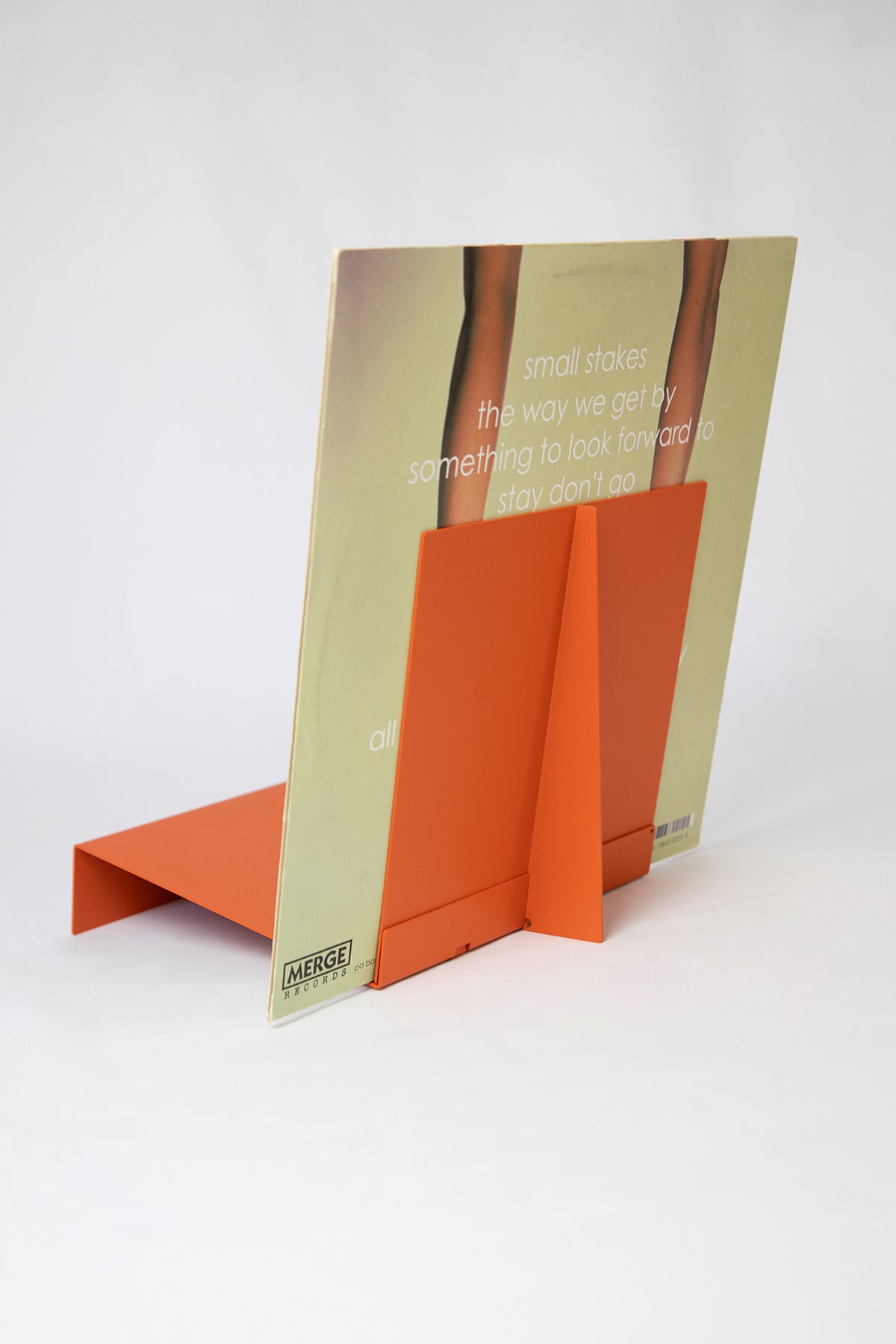 Upton LP Record Stand in burnt orange. Modern and minimalist tabletop steel vinyl record holder made for the storage, organization, and display 50 albums. Shown from the back holding an album on a white background.