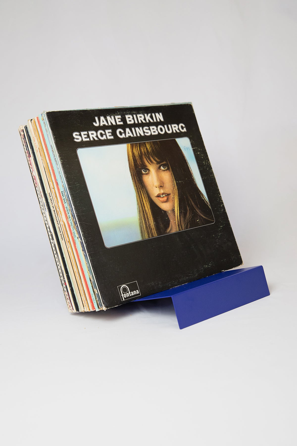 Upton LP Record Stand in cobalt blue. Modern and minimalist tabletop steel vinyl record holder made for the storage, organization, and display 50 albums. Shown here on a white background holding a vintage Jane Birkin / Serge Gainsbourg vinyl record album.