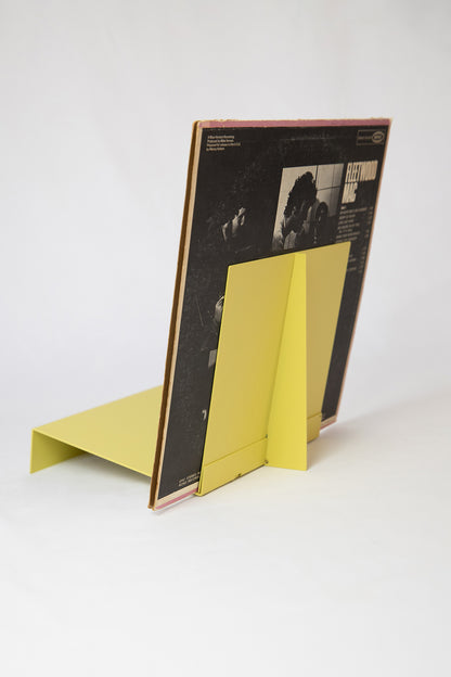 Upton LP Record Stand in pale yellow. Modern and minimalist tabletop steel vinyl record holder made for the storage, organization, and display 50 albums. Shown from the back on a white background holding an album sleeve.