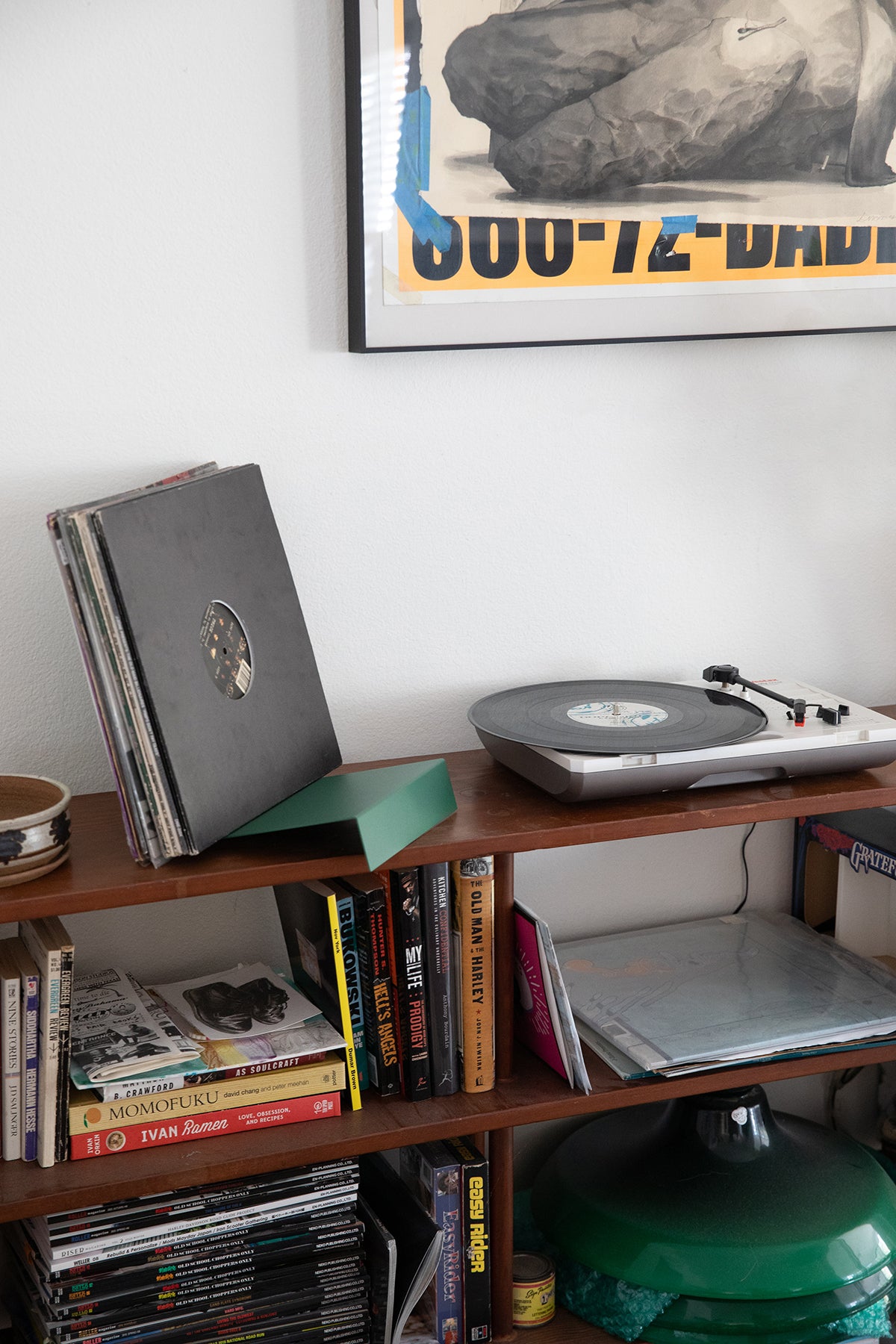 Upton LP Stand in pine green. Modern and minimalist tabletop steel vinyl record holder made for storage, organization, and display of 50 albums. Shown holding a stack of albums on a shelf with books and record player in an interior.