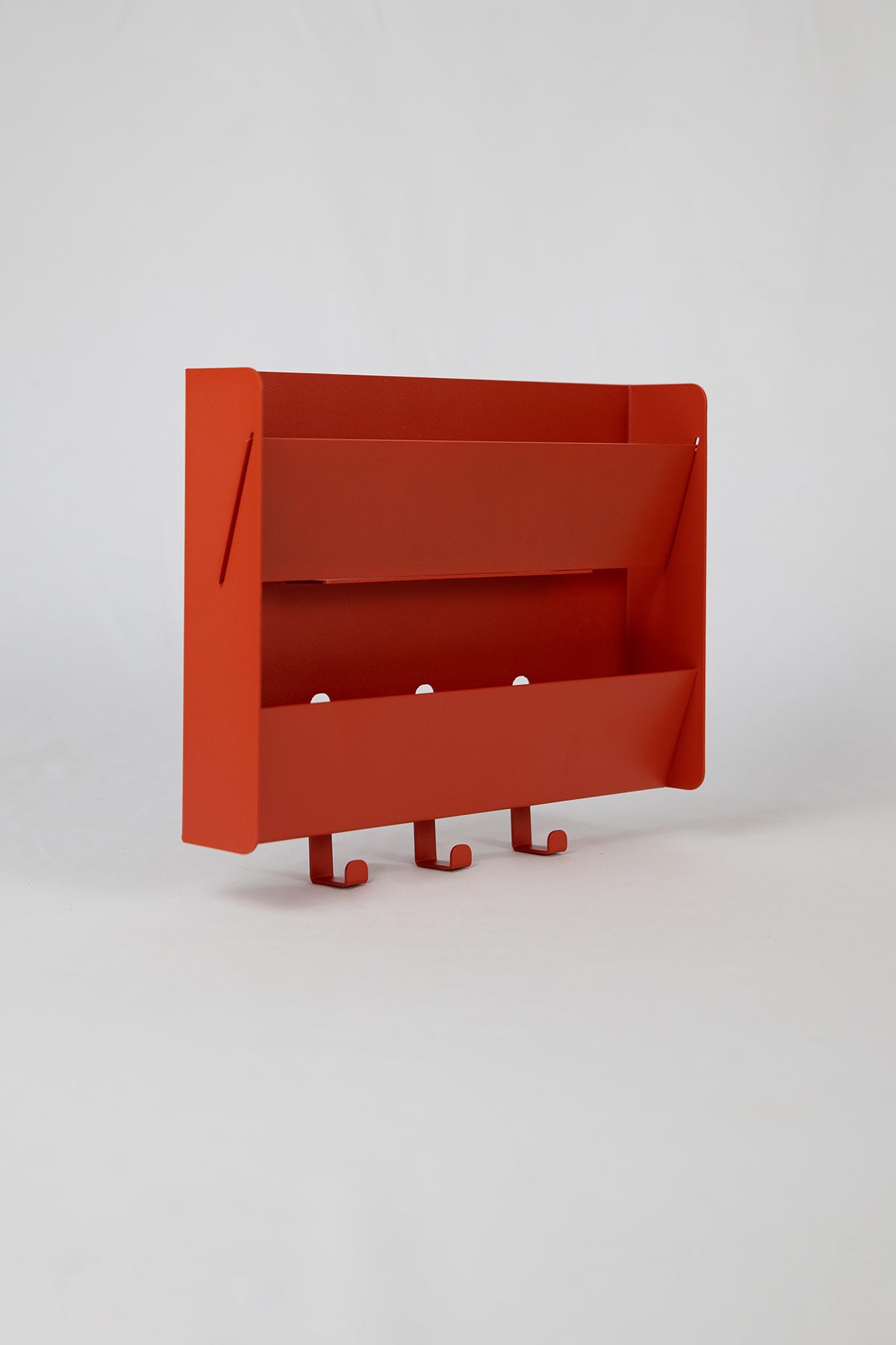 The Upton Mail Organizer in brick red (orange / red). Modern, minimalist, and design-forward wall-mounted mail organizer made of steel with a light yellow powder coat finish. Featuring two slots for mail and three sturdy hooks to hang keys, coats, bags, etc. Shown on a white background.