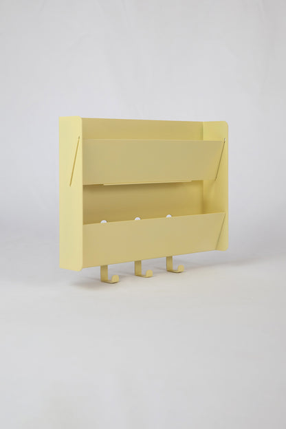 The Upton Mail Organizer in butter. Modern, minimalist, and design-forward wall-mounted mail organizer made of steel with a light yellow powder coat finish. Featuring two slots for mail and three sturdy hooks to hang keys, coats, bags, etc. Shown here on a white background.