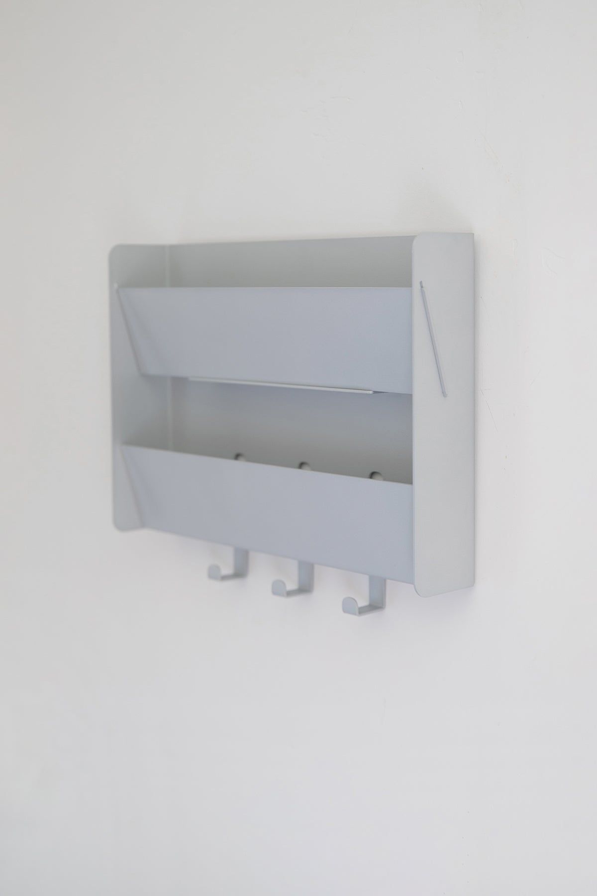 The Upton Mail Organizer in matte silver. Modern and design-forward wall-mounted mail organizer made of steel with a powder coat finish. Featuring two slots for mail and three sturdy hooks. Shown here on a white background.