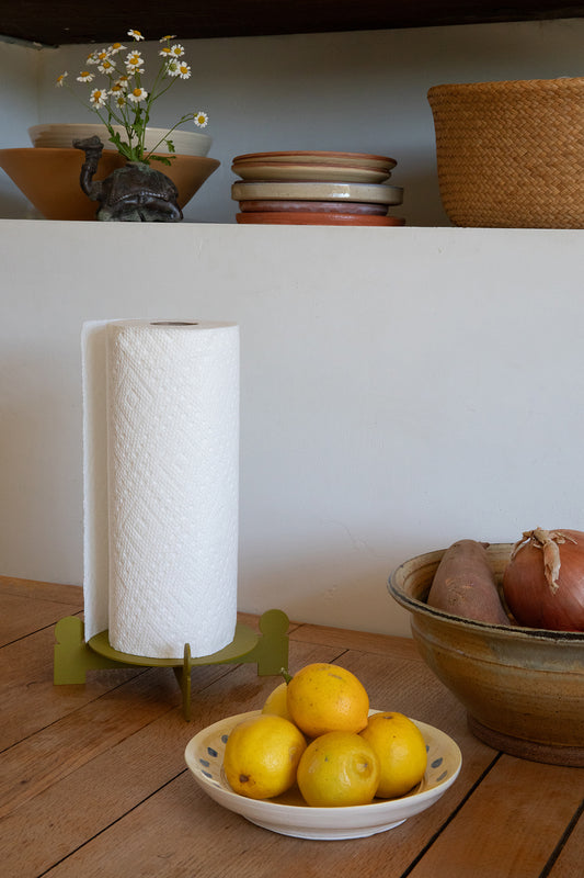 Upton Bal Paper Towel Holder in Olive. Sculptural metal paper towel holder with a roll of paper towels next to a bowl of lemons on a wooden table.