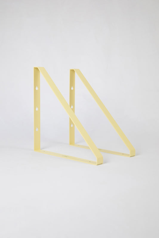 Upton Shelf Bracket Set in butter yellow. With a modern, minimalist design and made from powder coated steel, these slim triangle brackets are a unique home storage solution that adds character and color to your home. Shown on a white background.