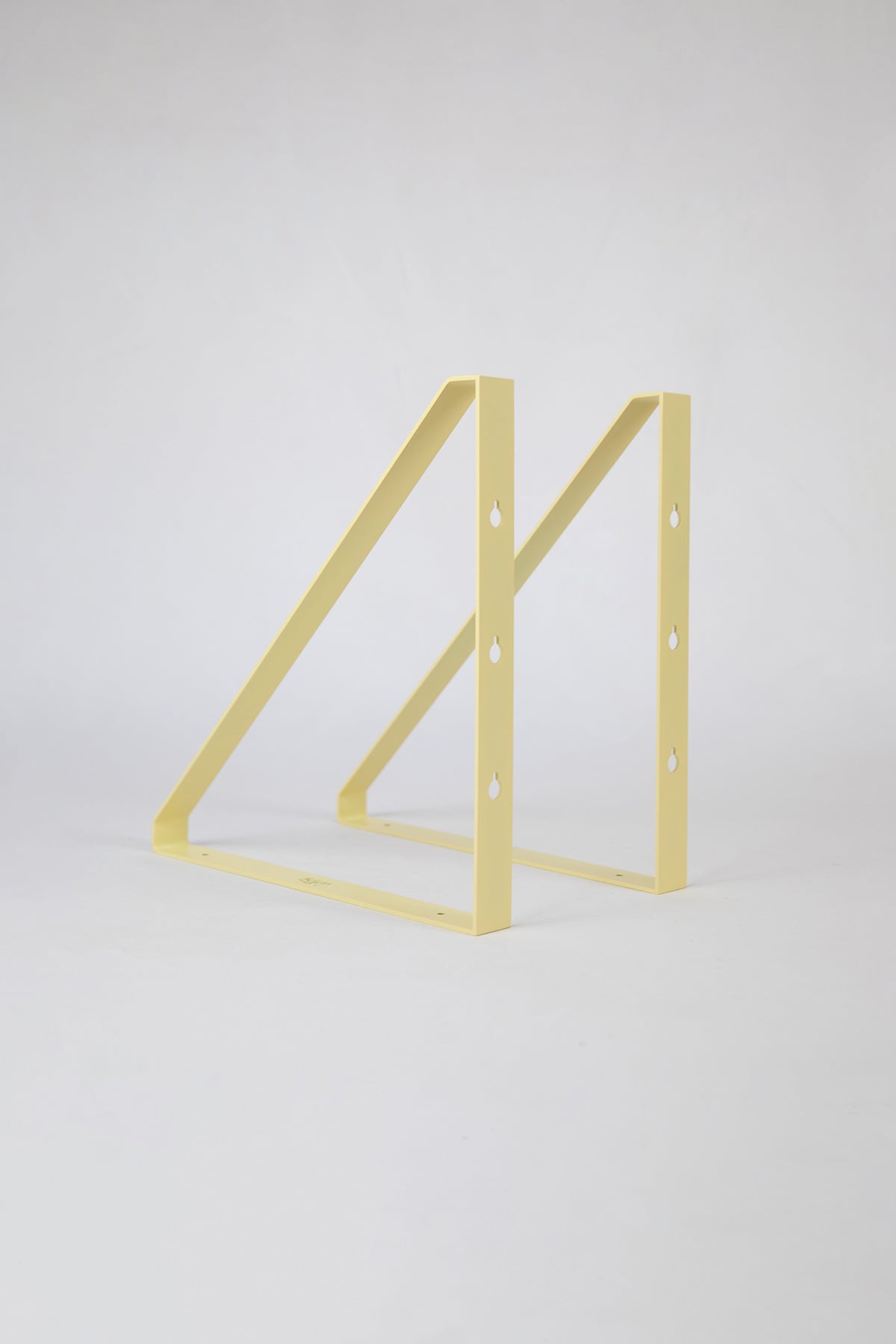 Upton Shelf Bracket Set in butter yellow. With a modern, minimalist design and made from powder coated steel, these slim triangle brackets are a unique home storage solution that adds character and color to your home. Shown on a white background.