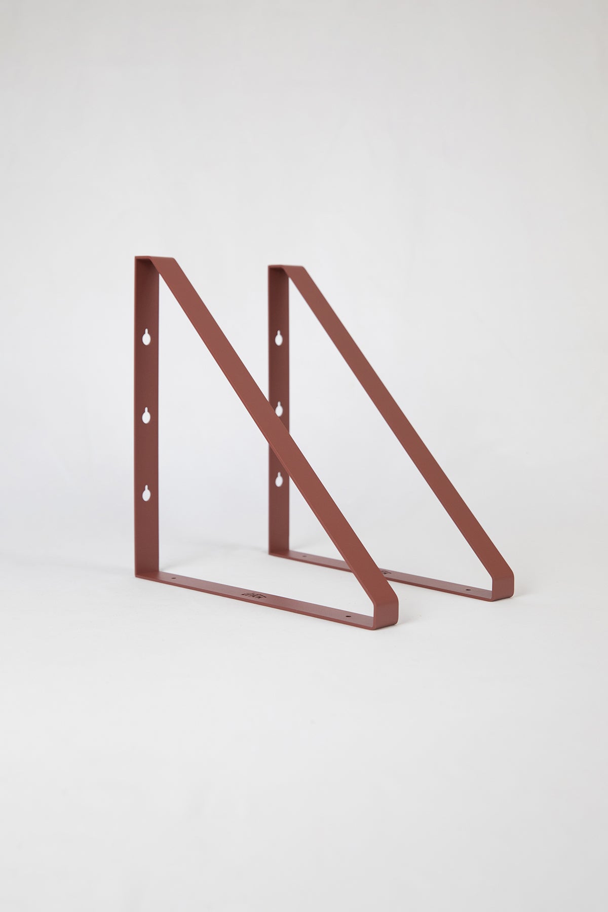Upton Shelf Bracket Set in rose (red/pink). With a modern, minimalist design and made from powder coated steel, these slim triangle brackets are a unique home storage solution that adds character and color to your home. Shown on a white background.
