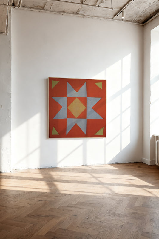 Quilt Stamp by Sunroom Studios x Upton, a custom framed art print on 100% cotton canvas. Large cut paper collage of a geometric starburst quilt pattern in terracotta red, light blue-gray, pale yellow, and olive green. Originally created as a risograph print. Shown on a white wall in a sunlit gallery room with wood herringbone flooring.