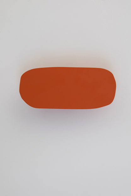 Upton Pill Wall Hook in burnt orange. A sculptural decorative steel wall hook with a burnt orange color scheme with a unique abstract shape, designed to hang bags, coats, towels, hats, and more. Shown here on a white background.